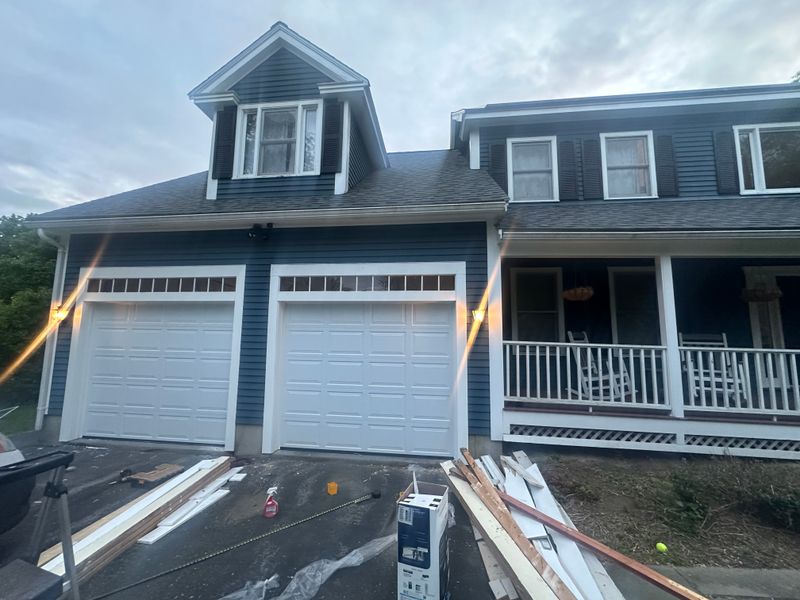 Newly installed dual white garage doors illuminated at dusk on blue colonial home