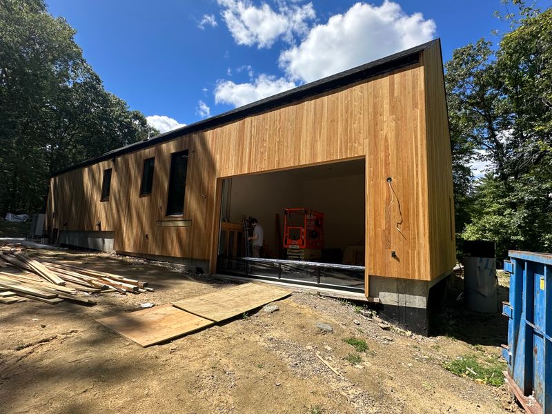 Modern cedar-clad building under construction with large garage opening