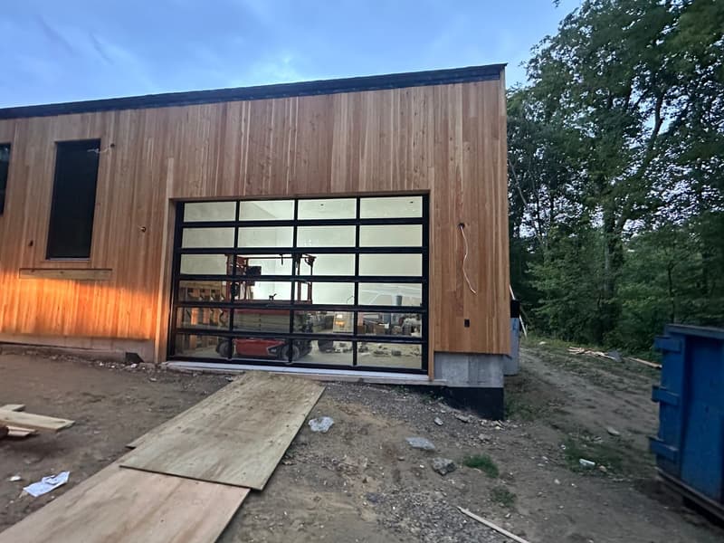Full-view glass garage door on modern cedar-clad building at dusk